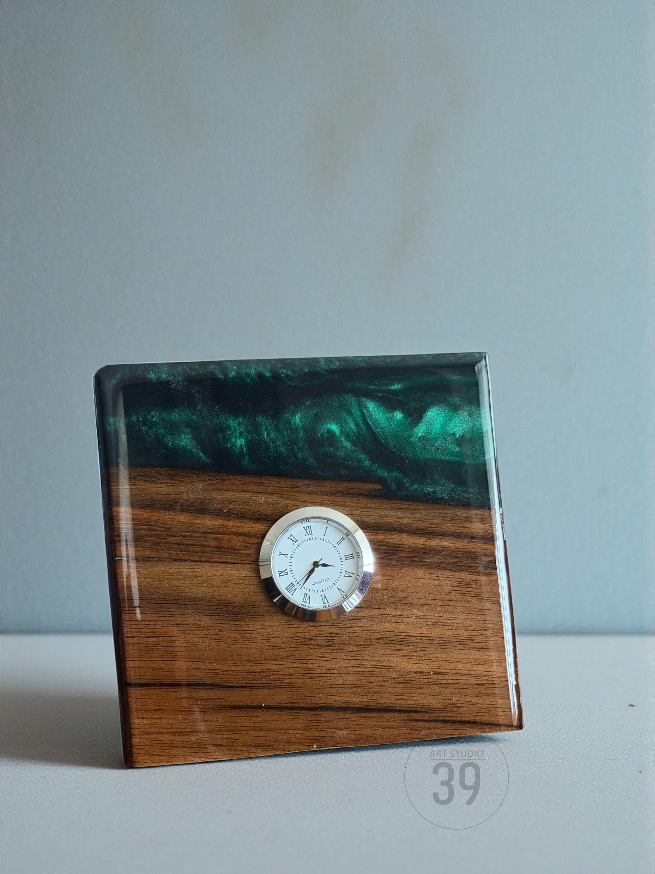 A wooden desk clock with a square shape. The bottom half is wood grain, and the top half is a dark green resin. A small, round clock face with Roman numerals is embedded in the wood. The clock is labeled "ART STUDIO 39".