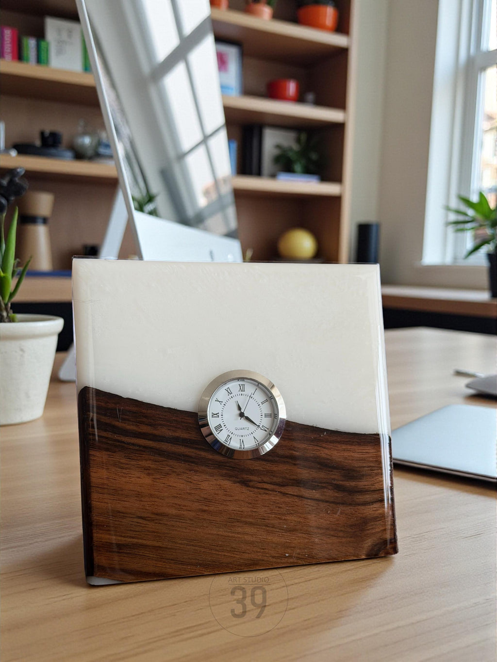 A rectangular desk clock with a silver-colored clock face and Roman numerals. The clock is set in a block of wood and white resin. The bottom half is dark wood, and the top half is white. The clock face is round.