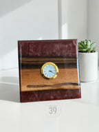 A square wooden clock with a gold-colored clock face and Roman numerals. The clock is set into a dark brown resin and wood base. The text "ART STUDIO 39" is printed on the bottom.