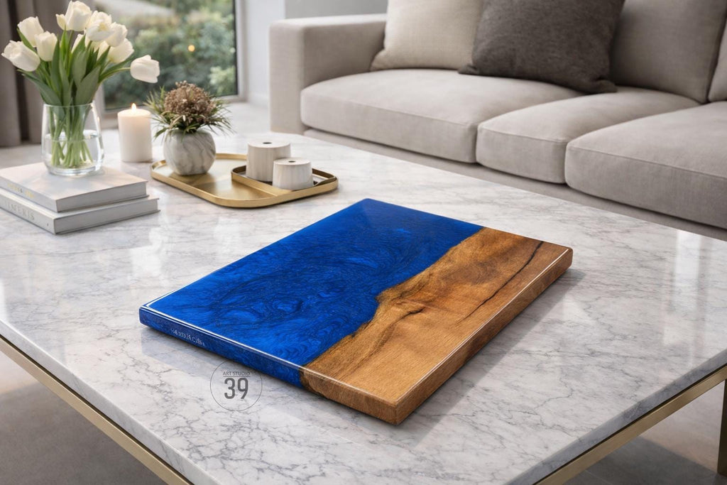 A rectangular wooden serving board with a vibrant blue epoxy resin section. The board has a natural wood grain on one side and a glossy blue finish on the other. The board is on a marble table.