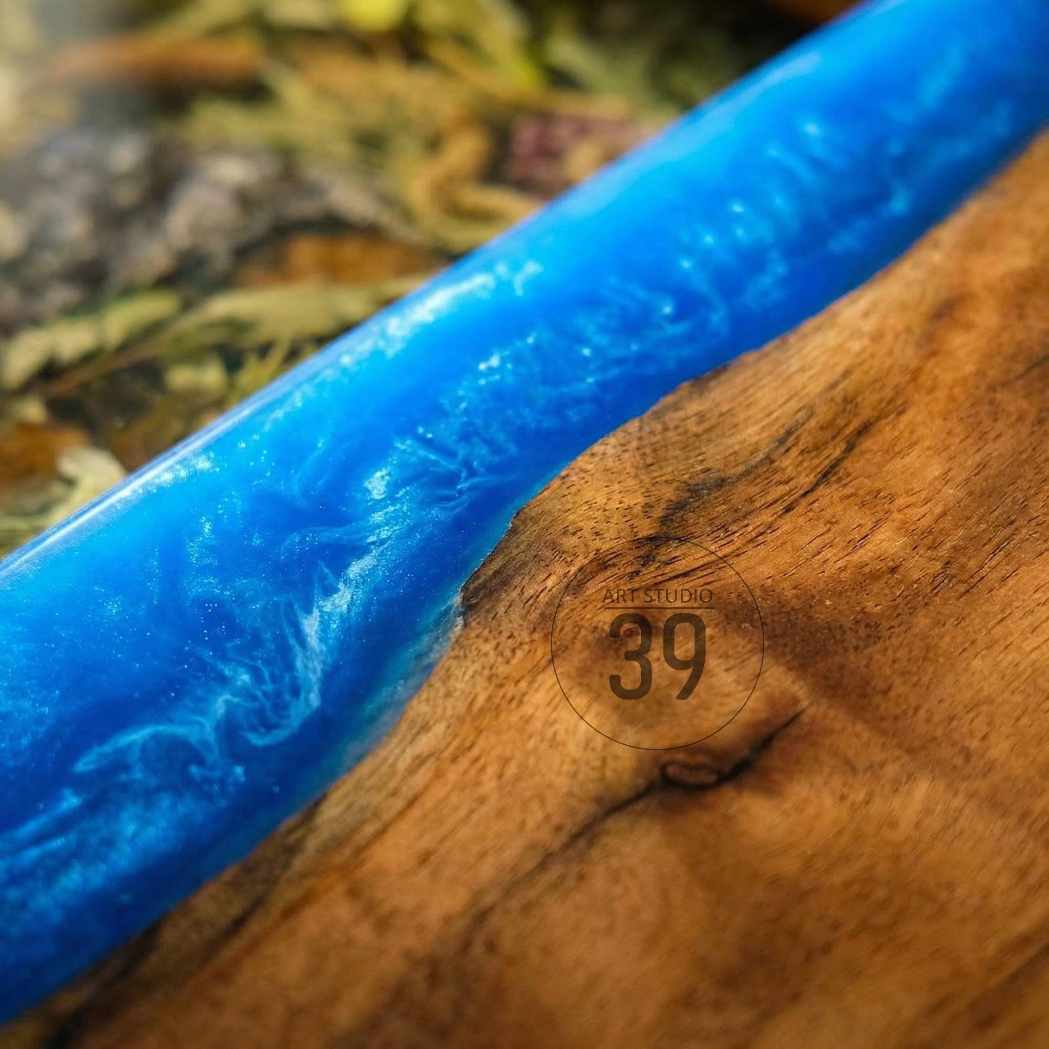 A close-up of a wooden surface with a vibrant blue resin inlay. The resin has a marbled effect with white swirls, creating a dynamic contrast against the wood grain. The text "ART STUDIO 39" is visible.