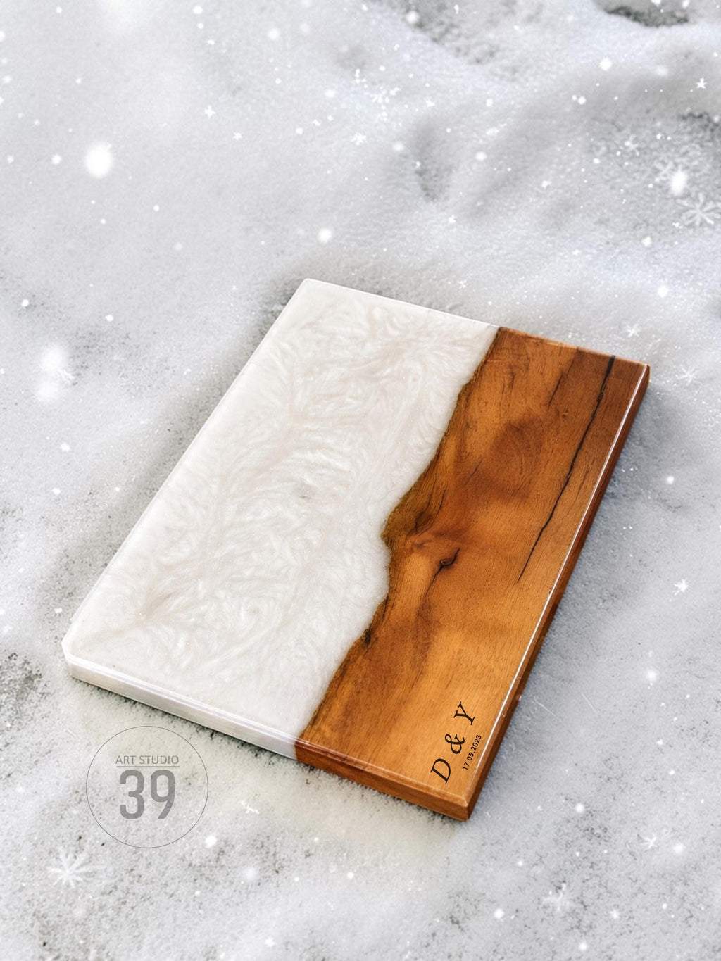 Rectangular wooden serving board with a white resin section. The wood is a warm brown color, and the resin has a swirling pattern. The initials "D &amp; Y" and the date "17.01.2023" are engraved on the wood. The board is a decorative item.