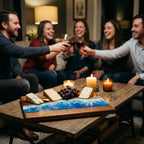 A wooden serving board with a blue and white resin wave design, holding cheese, crackers, and grapes. The board is on a rustic wooden table with lit candles. People are toasting with wine glasses in the background.