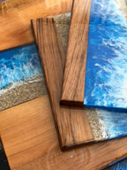 Wooden serving boards with a resin ocean wave design. The boards feature a combination of natural wood tones and vibrant blue and white resin, creating a coastal aesthetic. The boards are rectangular and have a smooth, glossy finish.