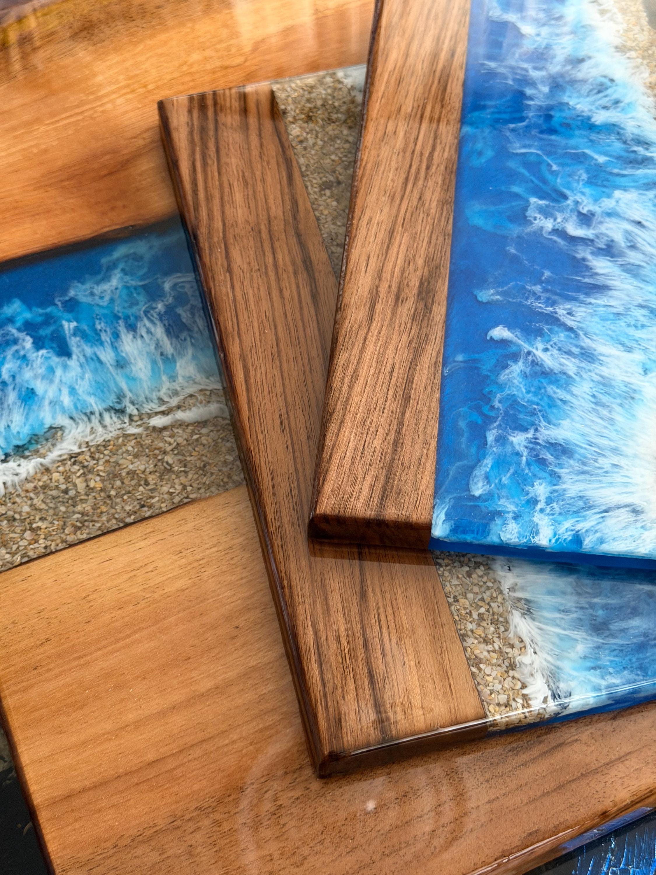 Wooden serving boards with a resin ocean wave design. The boards feature a combination of natural wood tones and vibrant blue and white resin, creating a coastal aesthetic. The boards are rectangular and have a smooth, glossy finish.