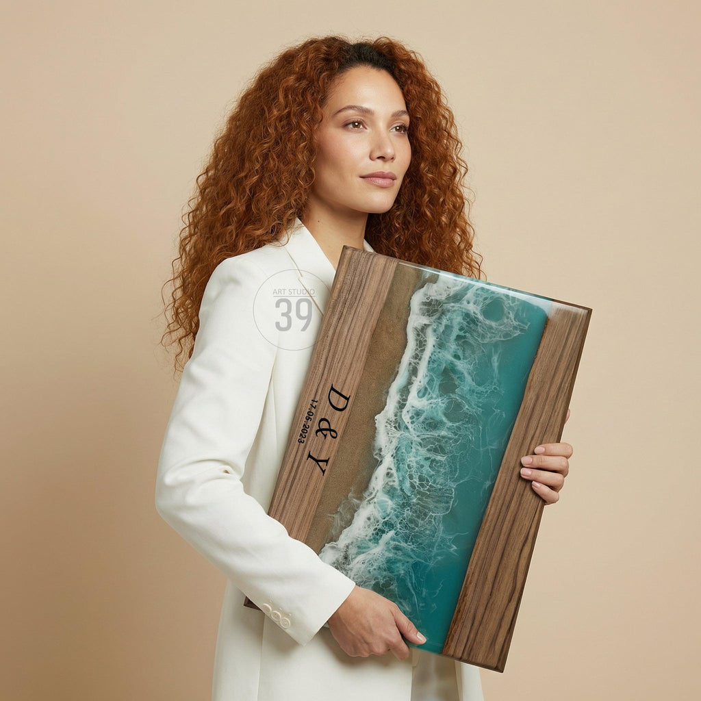 Wooden framed artwork featuring a beach scene with turquoise water and white waves. The artwork has a brown sand section and a dark wood frame. The initials "D &amp; Y" and the date "12.06.2023" are printed on the artwork.