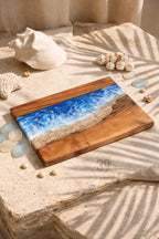 Wooden serving board with a resin ocean design. The board features a dark wood border, a sandy beach, and a blue and white wave design. The board is rectangular and has a glossy finish. The text "ART STUDIO 39" is visible.
