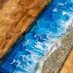 A wooden serving board with a resin ocean design. The board features a vibrant blue ocean with white foamy waves and a sandy beach. The text "ART STUDIO 39" is visible.