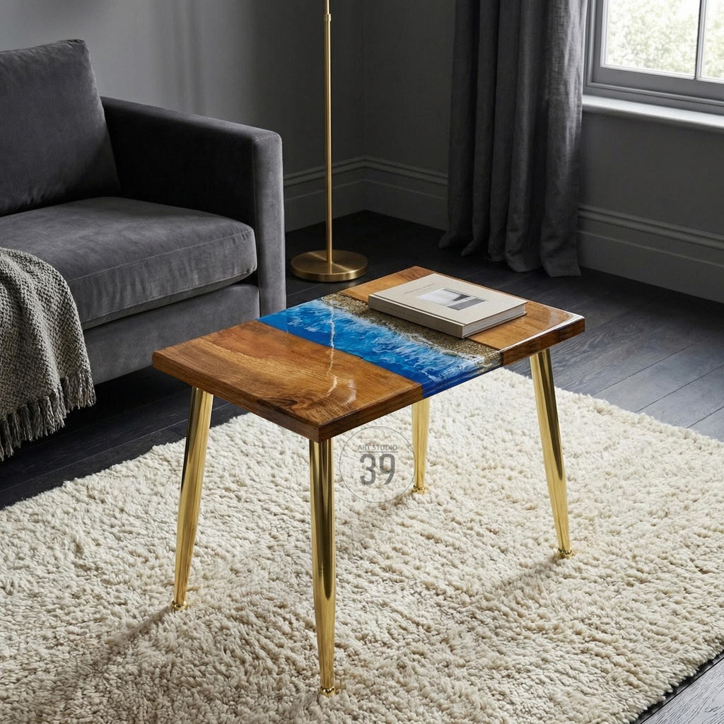 A square wooden side table with a blue resin river design and gold metal legs. The table has a natural wood grain finish and a rectangular book on top. The legs are approximately 16 inches tall.