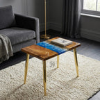 A square wooden side table with a blue resin river design and gold metal legs. The table has a natural wood grain finish and a rectangular book on top. The legs are approximately 16 inches tall.