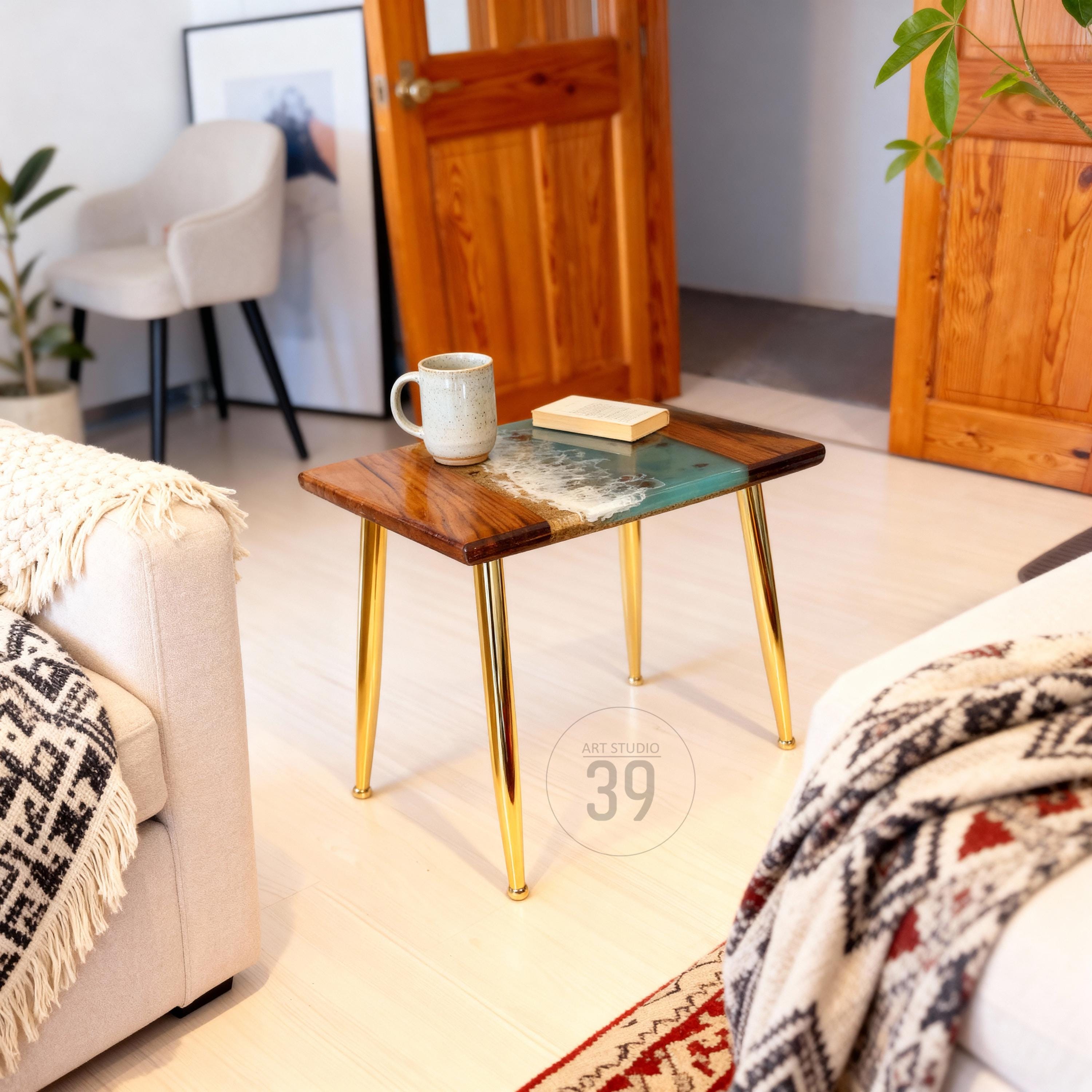A small, rectangular coffee table with a wooden top and gold-colored legs. The tabletop features a unique design with a wood grain pattern and a turquoise resin section. A mug and a book rest on the table. The table is approximately 20 inches long.
