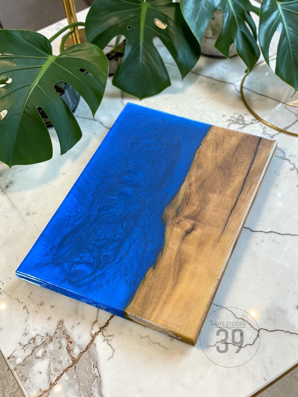 Rectangular wooden serving board with a vibrant blue resin section. The wood has a natural grain pattern, and the resin has a glossy finish. The board is likely used for serving food or as a decorative item.