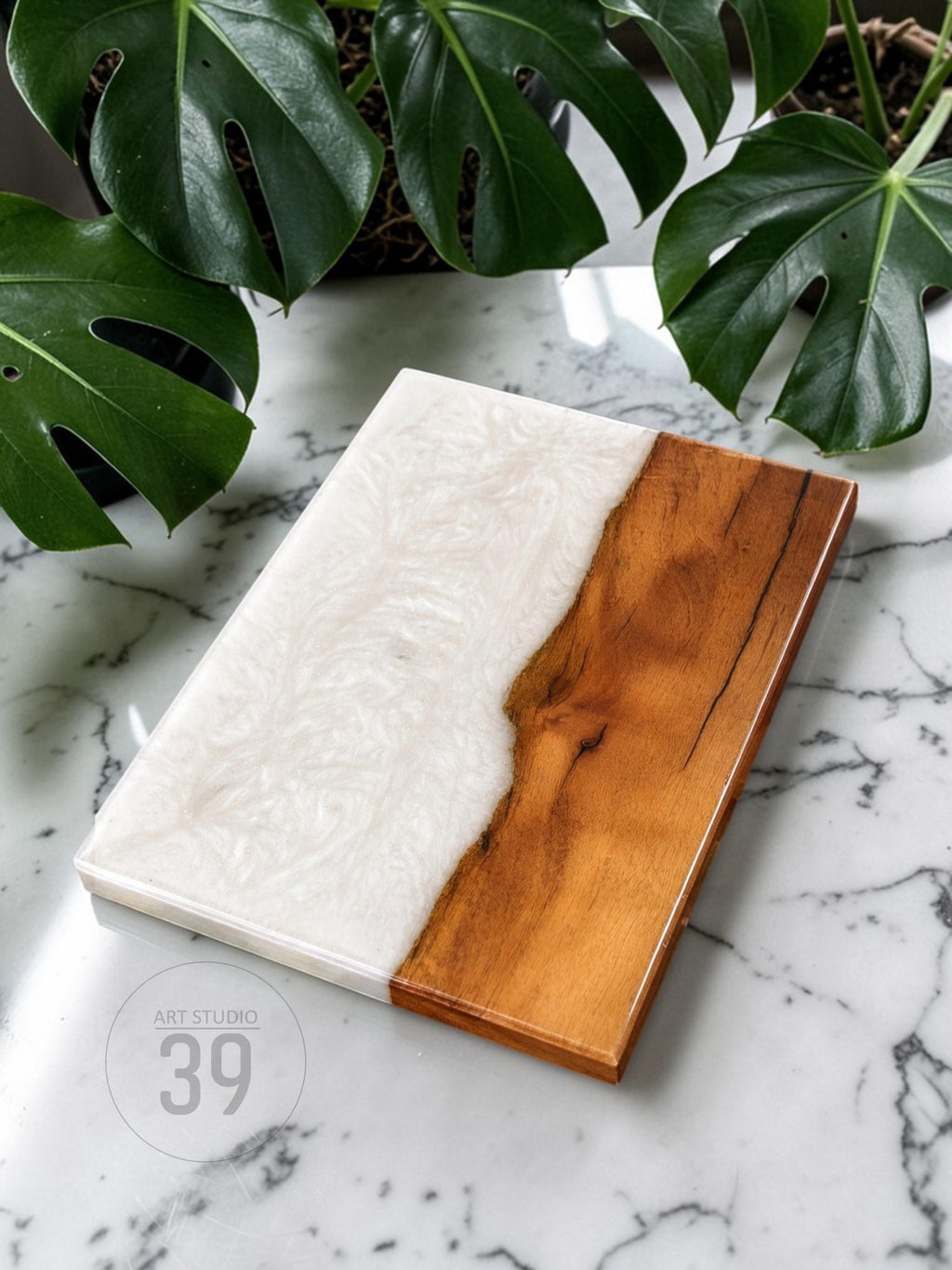 A rectangular serving board with a two-tone design. One half is a light wood grain, and the other is white resin with a swirling pattern. The board has a glossy finish and the text "ART STUDIO 39" is visible.
