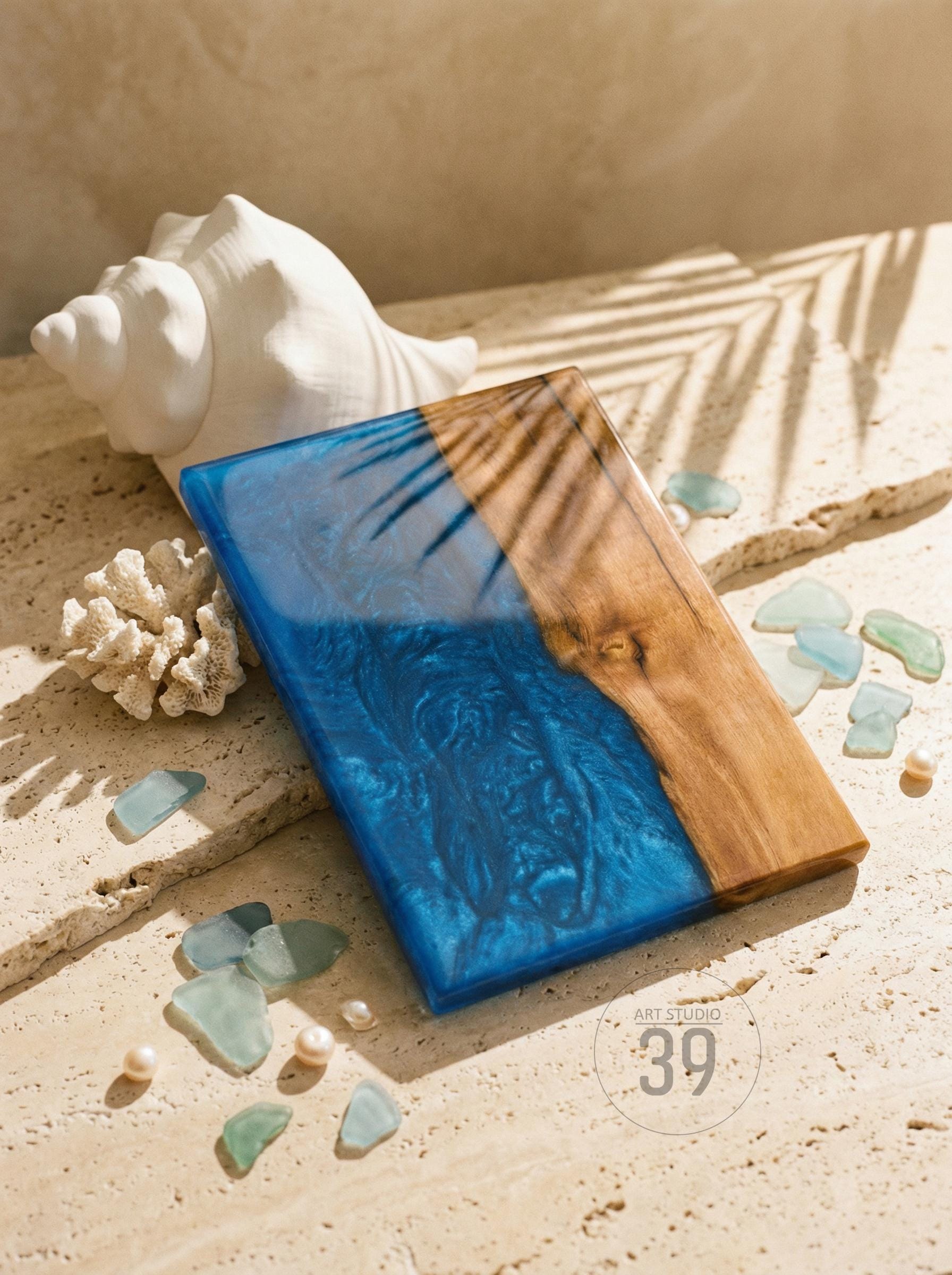 A rectangular wooden serving board with a blue resin design. The board is partially wood-grained and has a glossy finish. The words "ART STUDIO 39" are printed on the bottom right. Seashells and sea glass are scattered around the board.