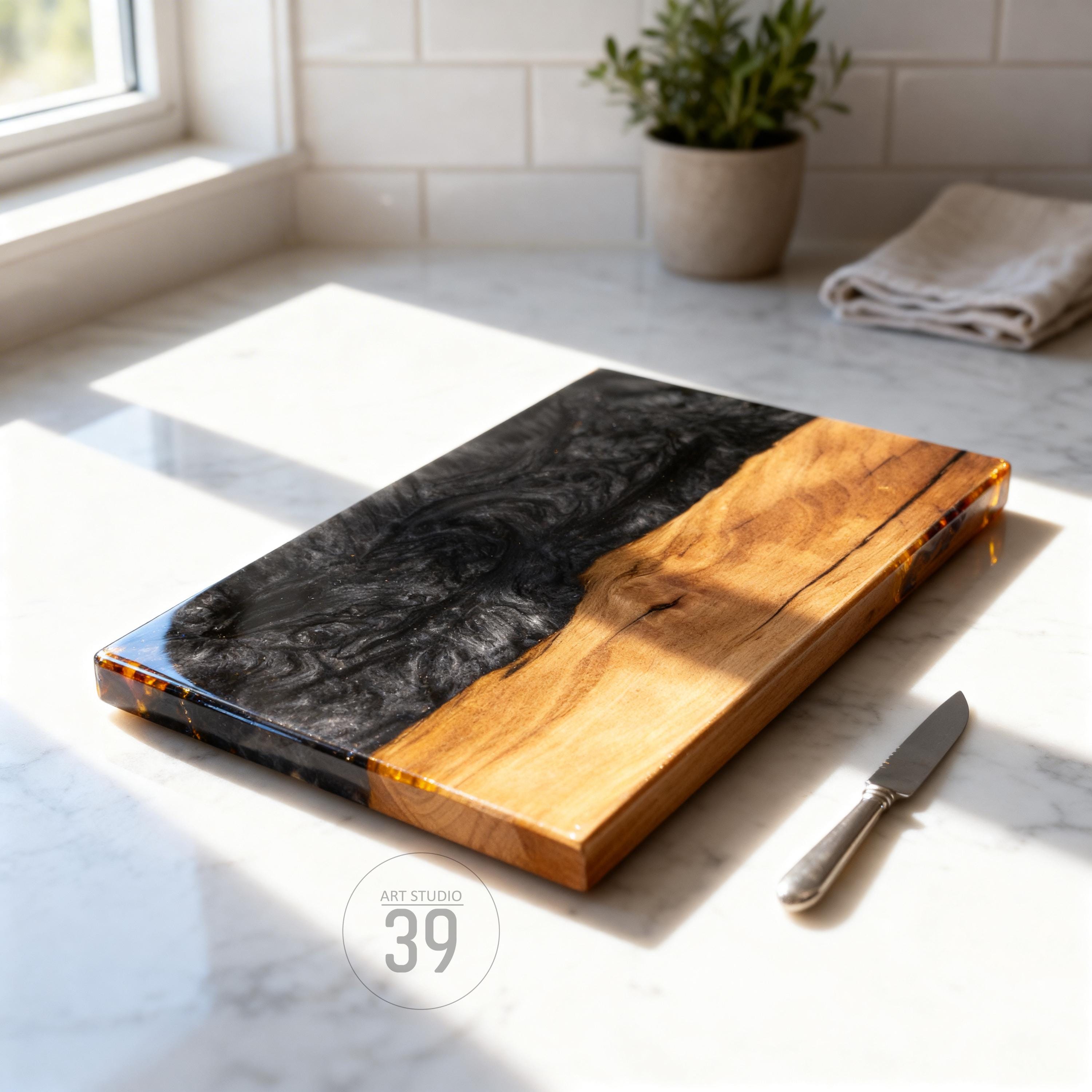 A rectangular wooden cutting board with a black resin section and a natural wood section. The board has a glossy finish and a small knife rests beside it. The logo "ART STUDIO 39" is visible.