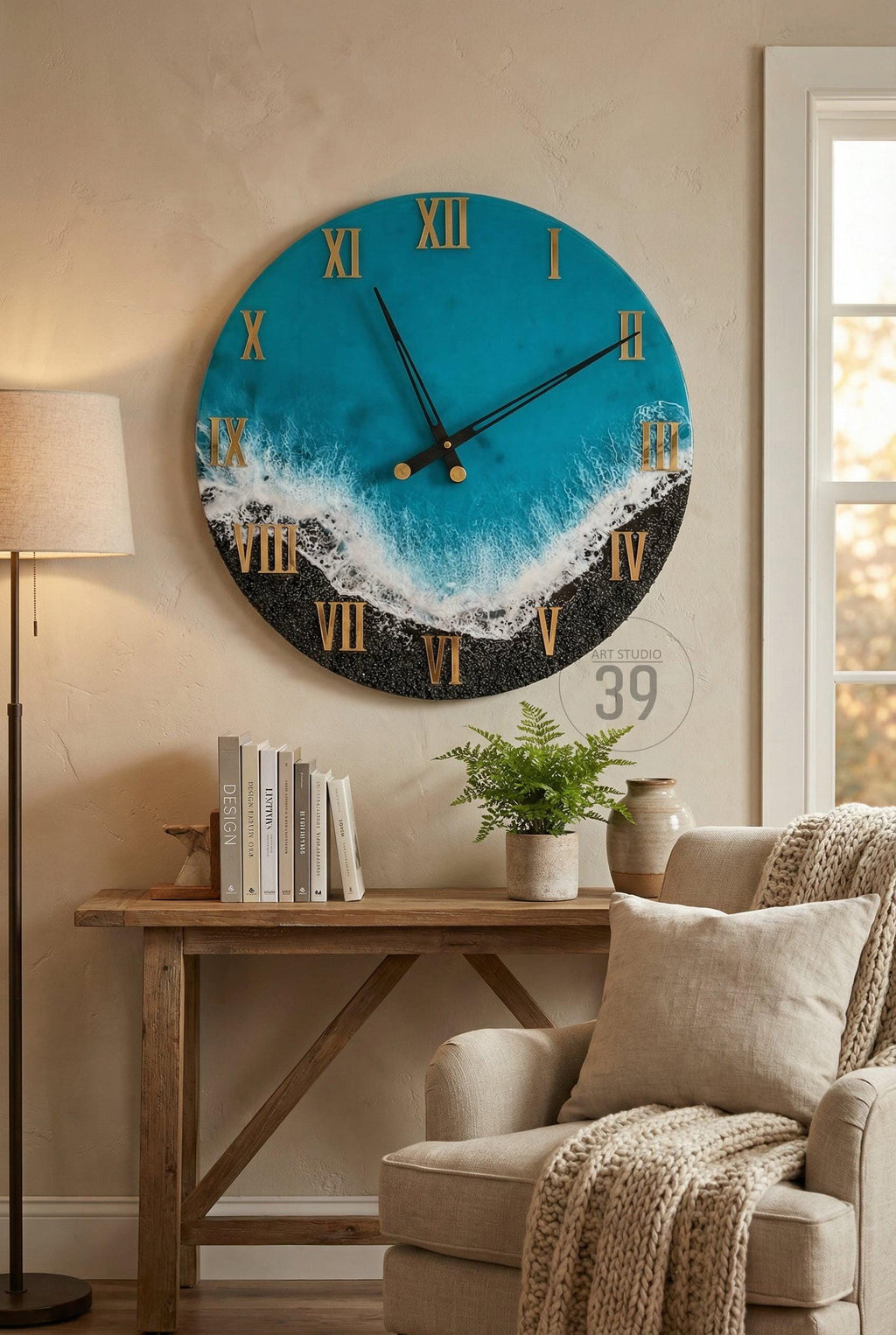 Large round wall clock with a blue and black ocean-themed design. The clock face features gold Roman numerals and hands. The clock is mounted on a beige wall above a wooden table.