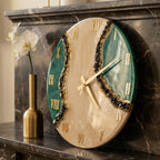 A round wall clock featuring a beige center and deep green sides separated by a textured black and gold geode-style accent. The clock face displays gold Roman numerals and thin gold hands, creating a high-contrast, layered appearance.