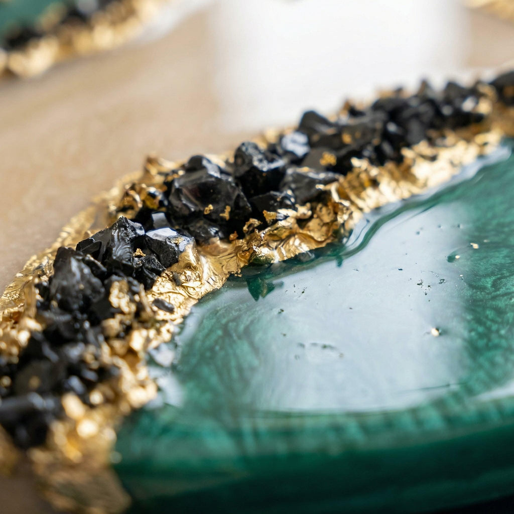 A decorative resin piece featuring a smooth, swirling emerald green surface contrasted by a textured border of jagged black stones and metallic gold leaf accents, creating a layered effect with a glossy, reflective finish throughout.