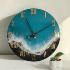 A round wall clock with a teal blue and black design, resembling a beach scene. The clock features gold Roman numerals and black clock hands. The clock is approximately 12 inches in diameter.