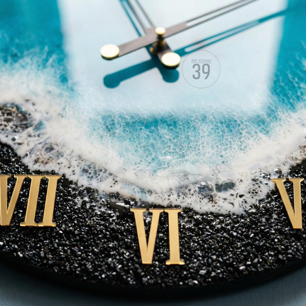 A round wall clock with a beach-themed design. The clock face features a black base with gold Roman numerals and a blue and white wave pattern. The clock hands are black with gold accents, and the text "ART STUDIO 39" is visible.