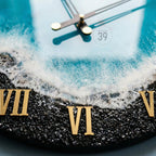 A round wall clock with a beach-themed design. The clock face features a black base with gold Roman numerals and a blue and white wave pattern. The clock hands are black with gold accents, and the text "ART STUDIO 39" is visible.