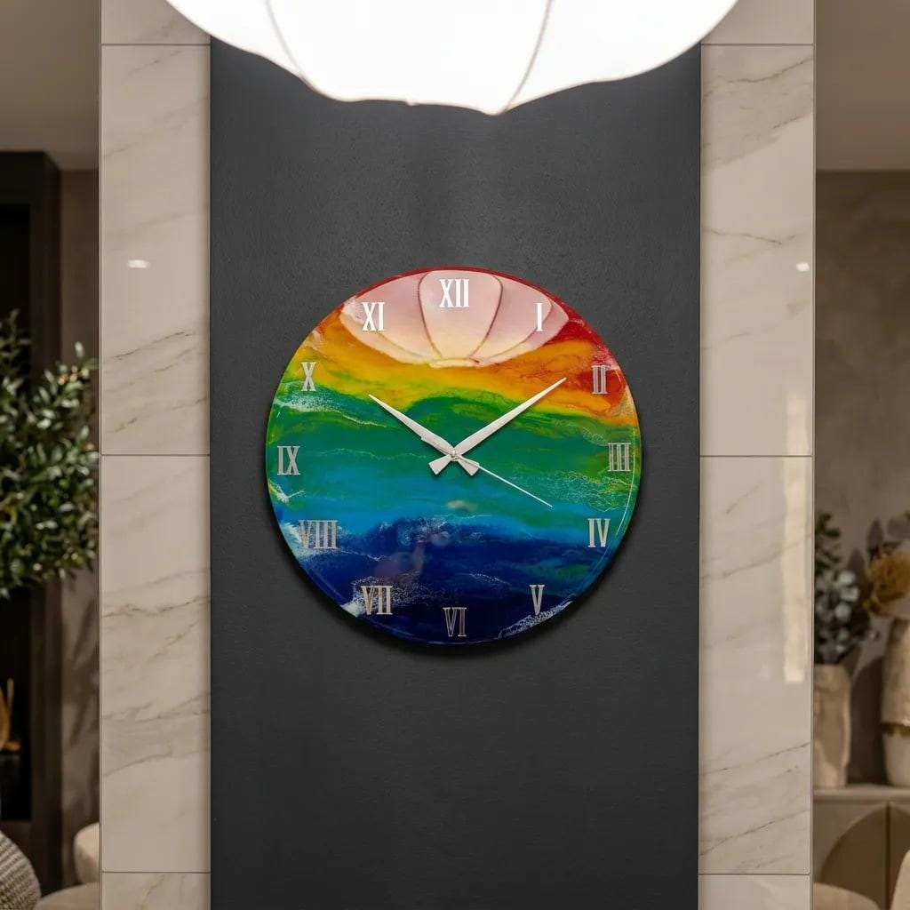 A round wall clock with a colorful, abstract design. The clock face features a rainbow of colors, with white Roman numerals and hands. The clock is mounted on a dark gray wall.