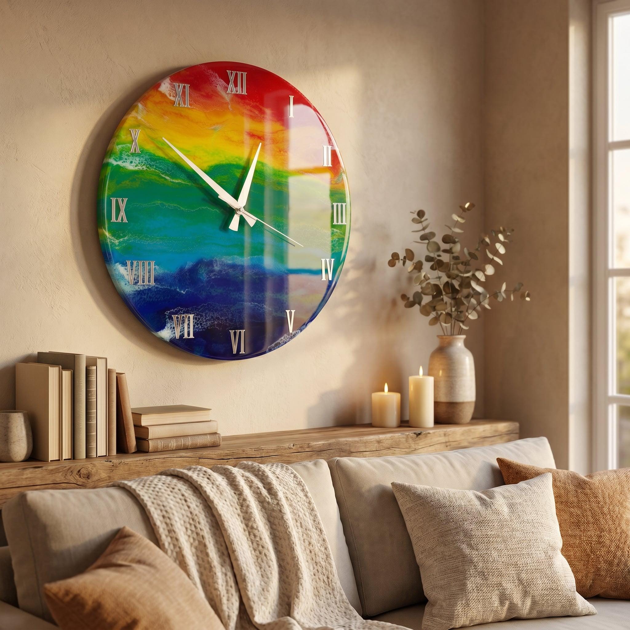 A large, round wall clock with a colorful rainbow design. The clock face features Roman numerals and white hands. The clock is mounted on a beige wall above a wooden shelf with books, candles, and a vase.