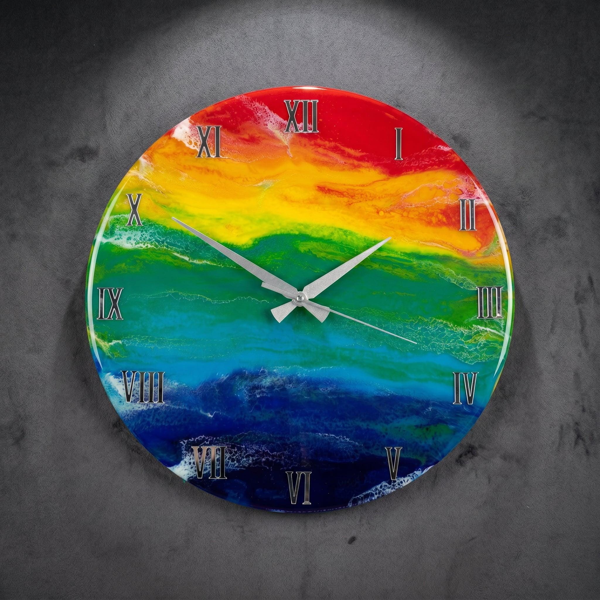 A round wall clock with a rainbow-colored face. The clock face features a gradient of colors, including red, yellow, green, blue, and purple. Silver Roman numerals mark the hours, and silver hands indicate the time.