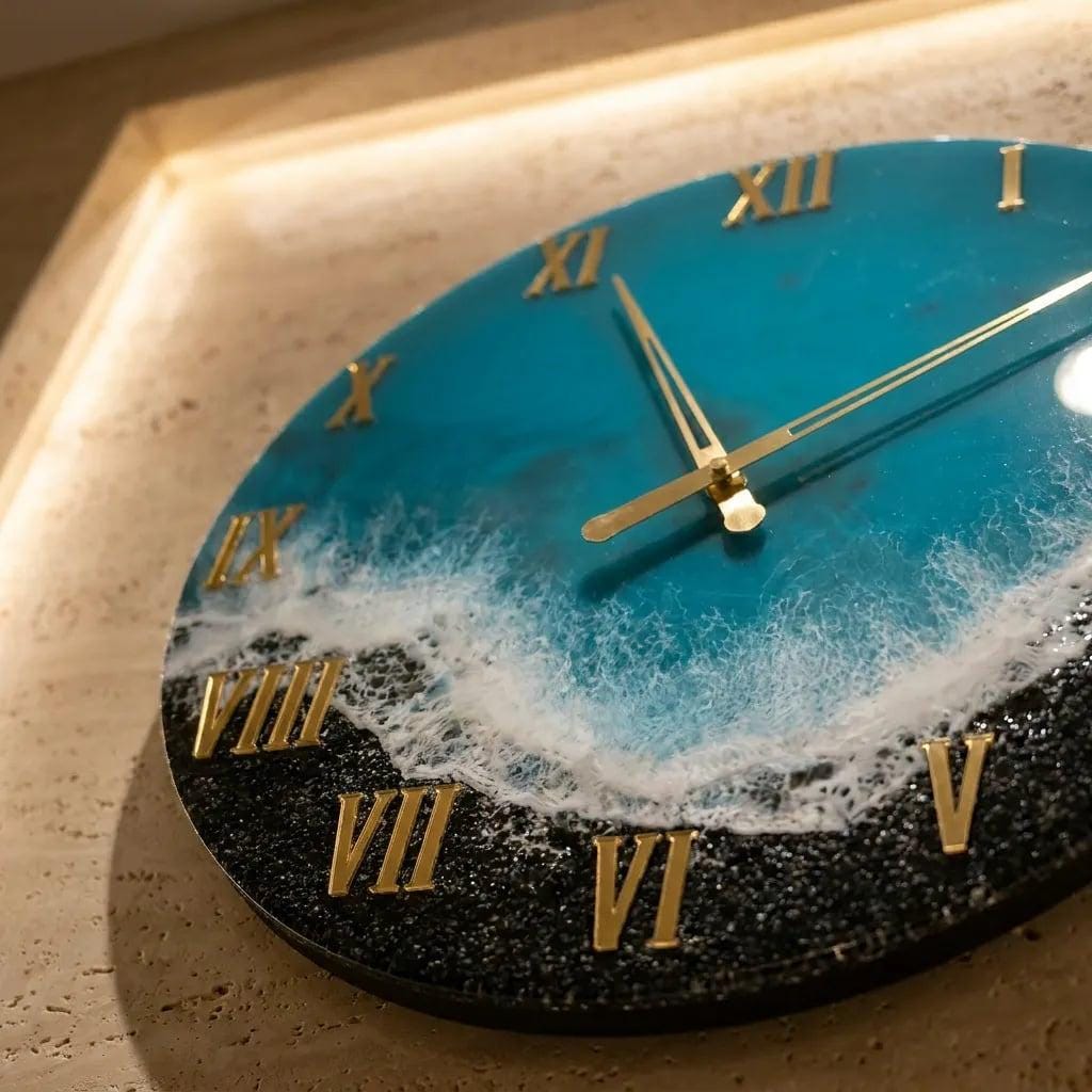 A round wall clock with a blue and white ocean-themed design. The clock face features gold Roman numerals and hands. The clock's design includes a black, textured border, and the clock is mounted on a beige wall.
