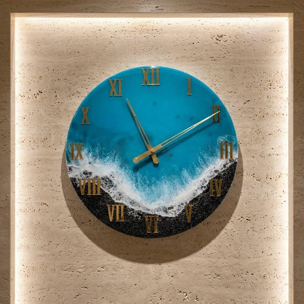 Round wall clock with a blue and white ocean wave design. The clock face features gold Roman numerals and gold hands. The clock is mounted on a beige wall.