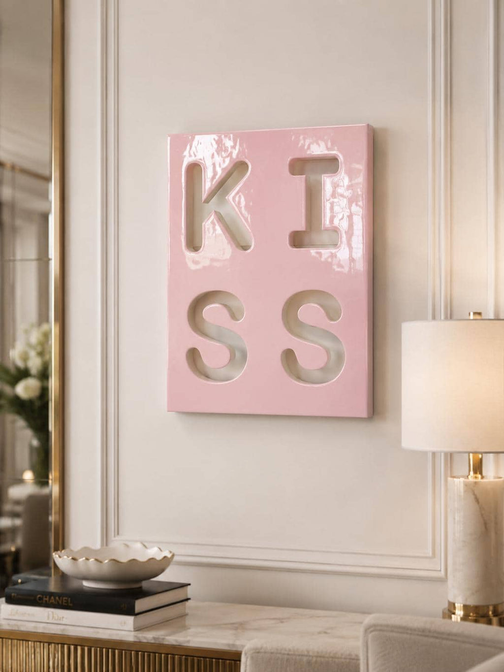 A rectangular, glossy, light pink wall art piece featuring the word KISS cut out in a bold, block-letter style. The letters are arranged in two rows of two, with K and I on the top row and S and S on the bottom row, creating a cutout effect.