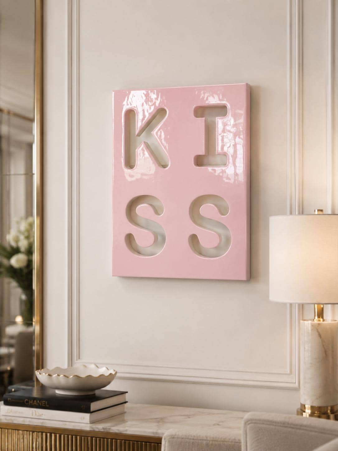 A rectangular, glossy, light pink wall art piece featuring the word KISS cut out in a bold, block-letter style. The letters are arranged in two rows of two, with K and I on the top row and S and S on the bottom row, creating a cutout effect.