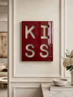 A rectangular wall art piece with a glossy deep red finish featuring the word KISS cut out in a bold, block-letter font. The letters are arranged in a two-by-two grid, with K and I on the top row and S and S on the bottom row.