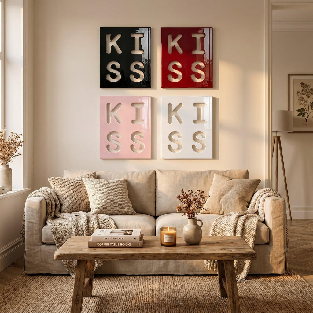 Four square wall art panels arranged in a grid, each featuring the word KISS in large, cut-out lettering. The top left panel is black, the top right is red, the bottom left is light pink, and the bottom right is white.