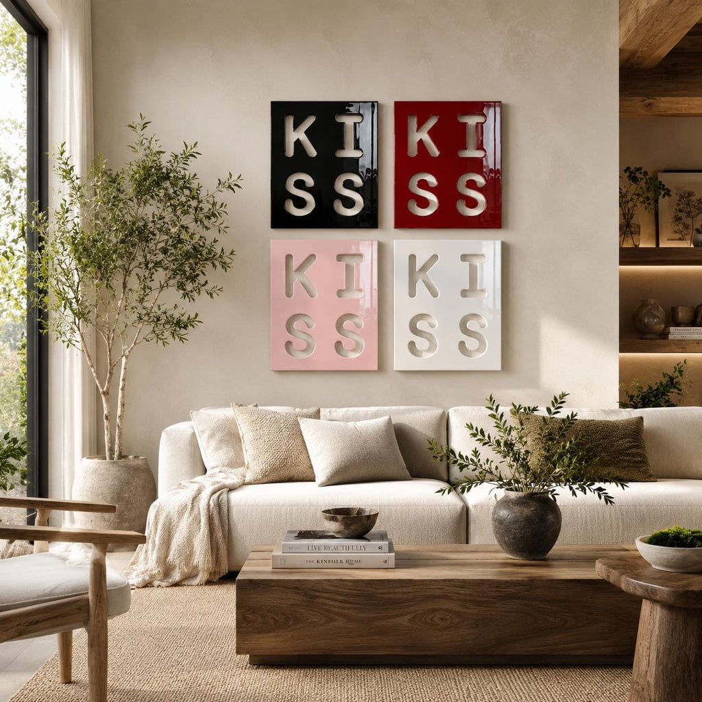 Four square wall art panels arranged in a grid, each featuring the word KISS in a cutout style. The top left panel is black, the top right is red, the bottom left is light pink, and the bottom right is white, all with a glossy finish.