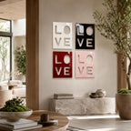 Four square wall art panels arranged in a grid, each featuring the word LOVE cut out in a bold, block-letter style. The panels are finished in glossy white, black, deep red, and soft pink, creating a modern, high-contrast display.