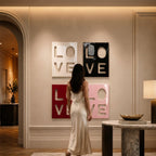 Four square wall art panels featuring the word LOVE in a stacked block letter design. The top left panel is white, the top right is black, the bottom left is deep red, and the bottom right is light pink, all with a glossy finish.