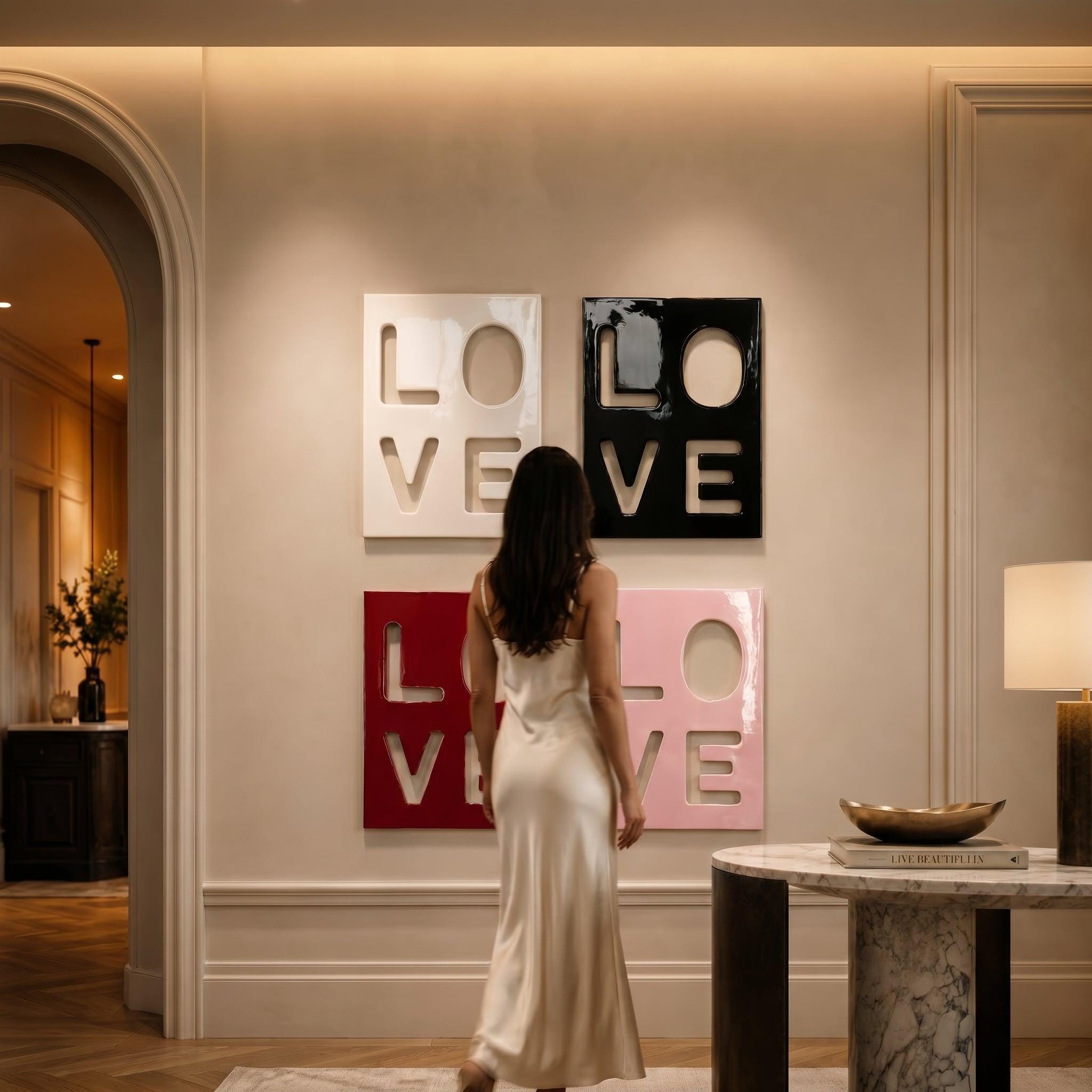 Four square wall art panels featuring the word LOVE in a stacked block letter design. The top left panel is white, the top right is black, the bottom left is deep red, and the bottom right is light pink, all with a glossy finish.