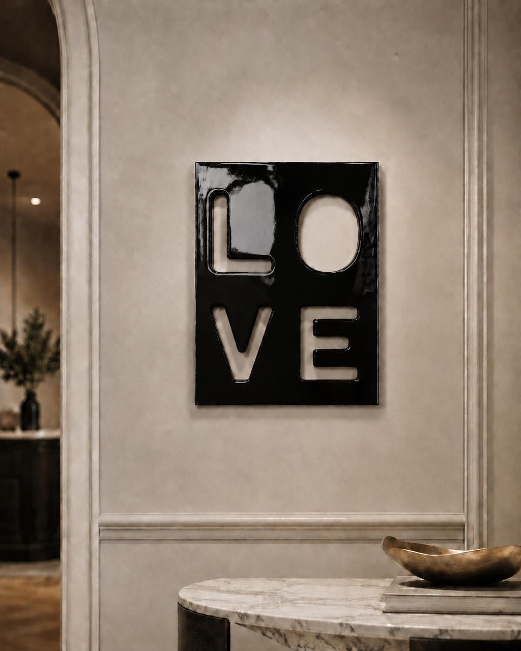 A rectangular black wall art piece featuring the word LOVE cut out in a bold, block-letter style. The glossy surface of the black panel contrasts with the negative space of the letters, which reveal the wall color behind the artwork.