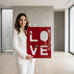A rectangular, glossy, deep red sign featuring the word LOVE cut out in large, bold, white block letters. The sign has a smooth, reflective surface and is held upright, displaying the four letters arranged in a two-by-two grid format.