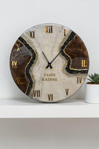 A circular wall clock with a marbled white and brown resin face featuring black glitter accents, gold Roman numerals, and black hands. The name YASIN KAZDAL is printed in gold lettering in the center of the clock face.