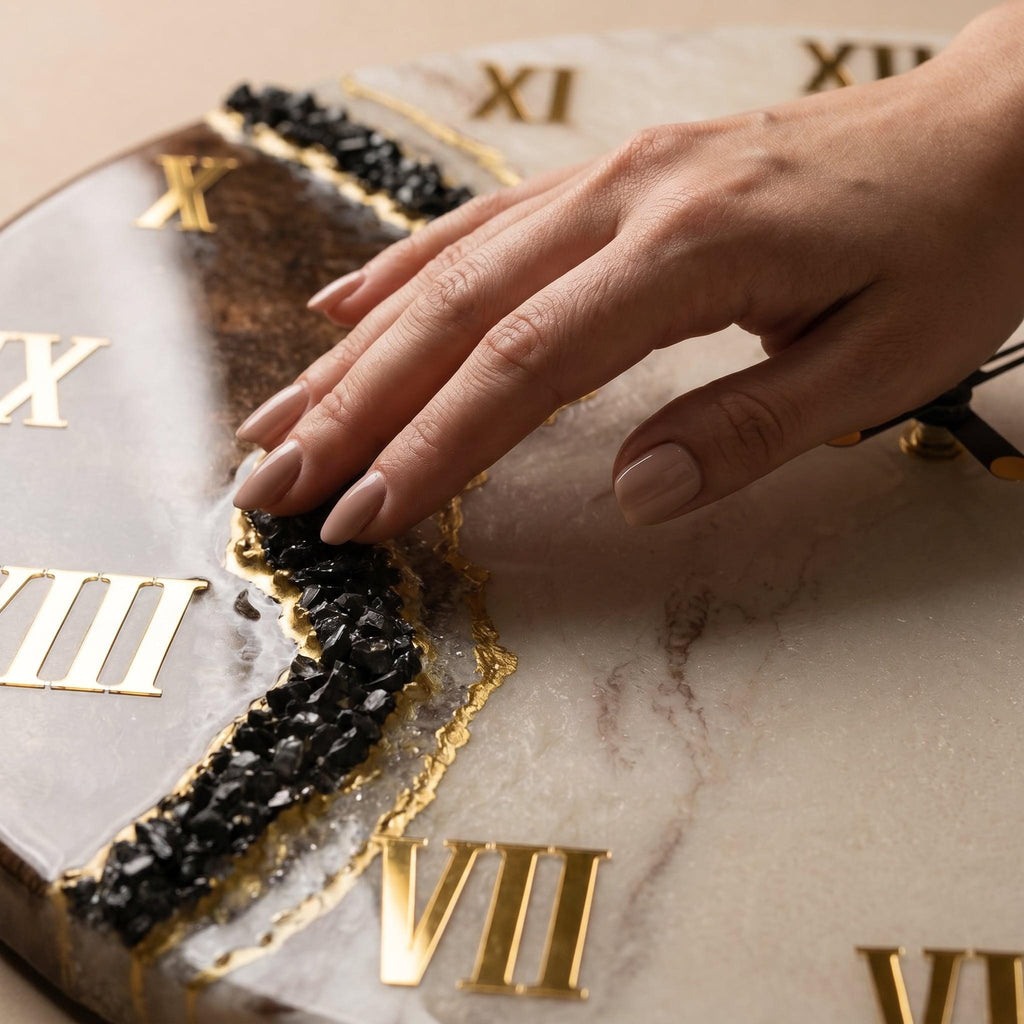A round wall clock featuring a white and brown marbled surface with gold Roman numerals. A jagged, textured band of black crushed stone runs diagonally across the face, accented with a thin gold leaf border and black clock hands.
