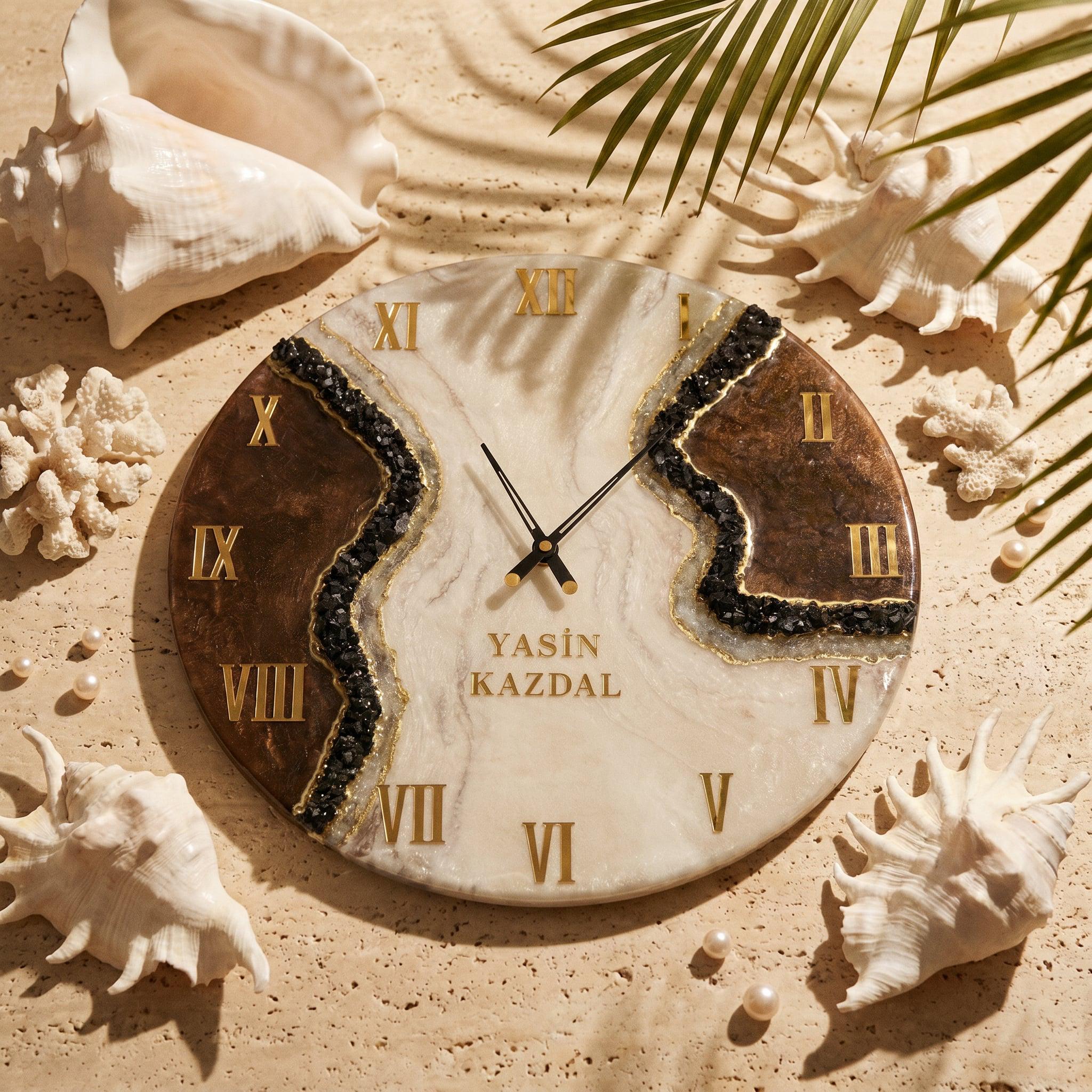 A round wall clock with a white and brown marbled surface, featuring gold Roman numerals and black clock hands. A central band of black crushed stone accents the face, which displays the text YASIN KAZDAL in gold lettering.