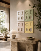 Four square wall art panels arranged in a grid, each featuring the embossed letters C, I, C, I, A, O. The top-left panel is white, the top-right is light green, the bottom-left is light pink, and the bottom-right is light yellow.