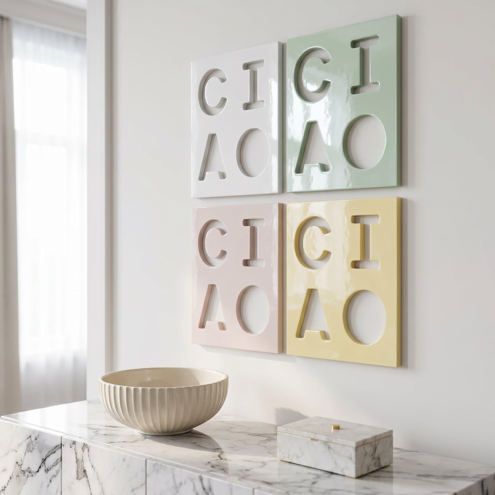 Four square wall panels arranged in a grid, each featuring cut-out letters spelling CIAO. The top-left panel is white, top-right is sage green, bottom-left is pale pink, and bottom-right is pale yellow, all with a glossy finish.