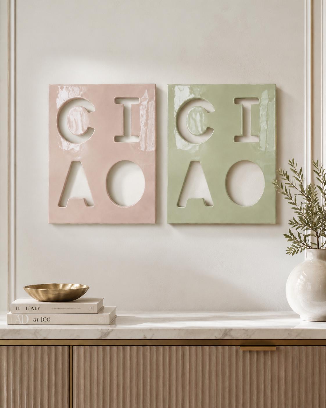 Two rectangular wall plaques featuring cut-out letters spelling CIAO. One plaque is a glossy pastel pink, and the other is a glossy sage green. Each plaque displays the letters C, I, A, and O arranged in a two-by-two grid pattern.