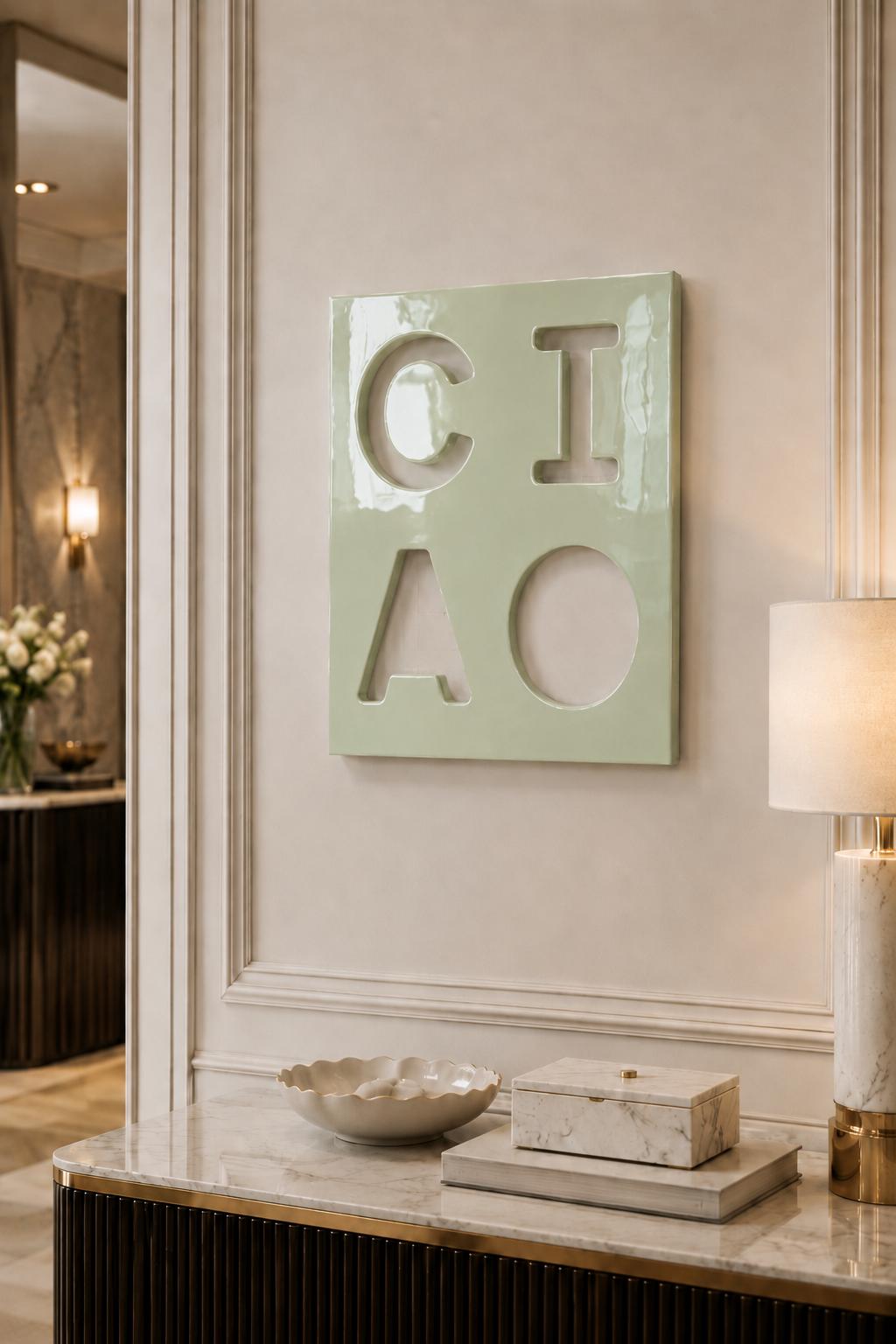 A square, light green wall plaque featuring the cutout letters C, I, A, and O arranged in a two-by-two grid. The surface of the plaque has a glossy, reflective finish, and the letters are formed by negative space against the wall.
