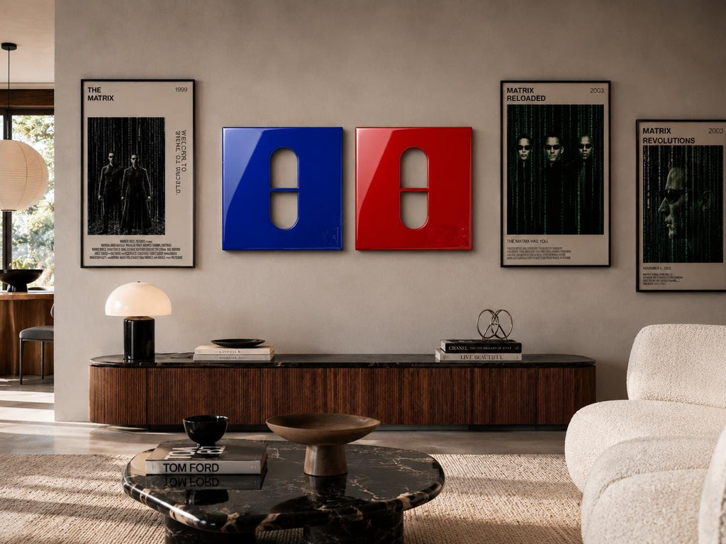 Two square wall art pieces featuring a glossy blue panel and a glossy red panel, each with a central vertical pill-shaped cutout. These are displayed on a wall alongside three framed movie posters for The Matrix, Matrix Reloaded, and Revolutions.