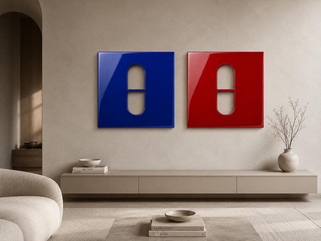 Two square wall art panels, one deep blue and one vibrant red, each featuring a central cutout in the shape of a pill or capsule. The panels have a smooth, glossy finish and are mounted side-by-side on a neutral-toned wall surface.