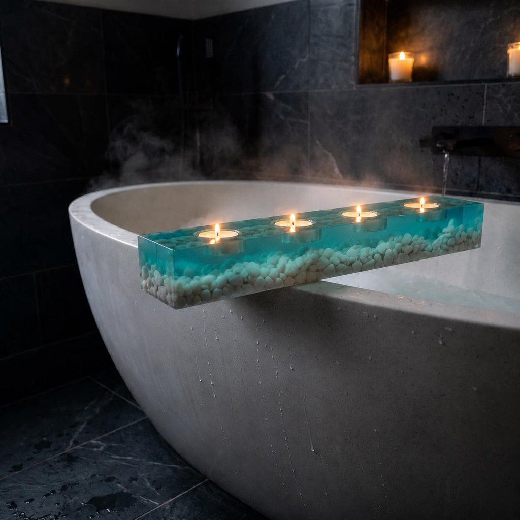 A rectangular bath tray made of clear resin with a turquoise blue tint, filled with small white pebbles at the base. The tray features four circular indentations, each holding a small lit tea light candle with a warm yellow flame.